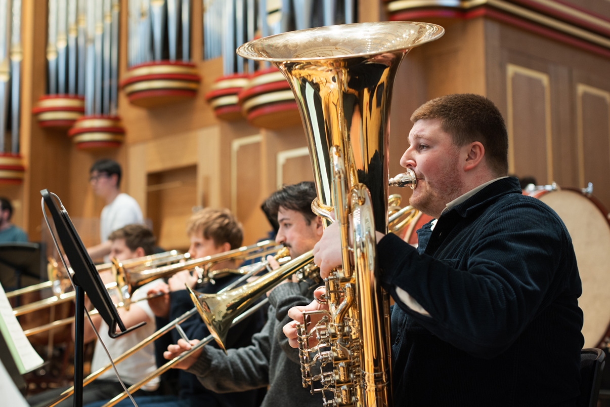 Brass students playing their instruments in a orchestra rehearsal.
